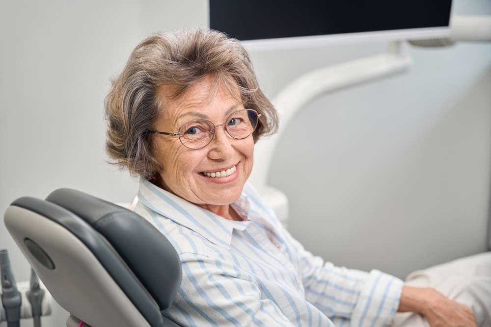 Image of a dentist holding different types of "fake teeth" - dentures, partials, and an implant - while consulting with a patient in a modern dental office. No text on image.